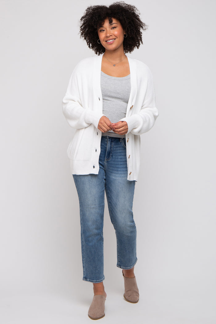 woman wearing a white knit cardigan over a gray tank top, paired with light blue jeans and beige slip-on shoes