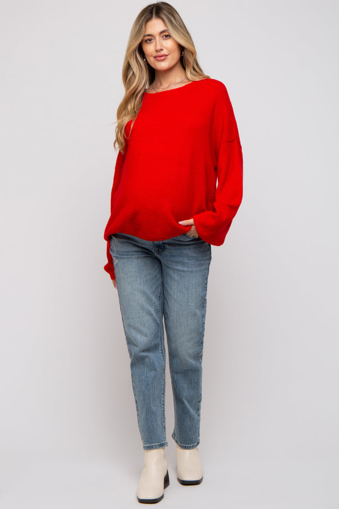 woman wearing a red oversized sweater and light blue straight leg jeans, styled casually in maternity wear