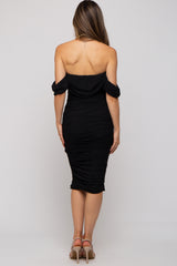woman wearing a black off-the-shoulder maternity dress with ruched detail, showing a fitted silhouette from the back