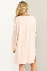 woman wearing a light pink oversized sweater dress with side slits and long sleeves, viewed from the back
