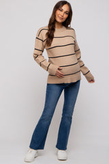 woman wearing a tan striped maternity sweater and blue flared jeans, holding her baby bump