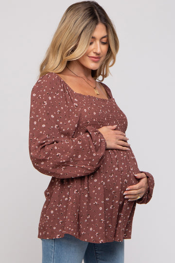 woman wearing a rust floral maternity top with puffed sleeves and holding her baby bump