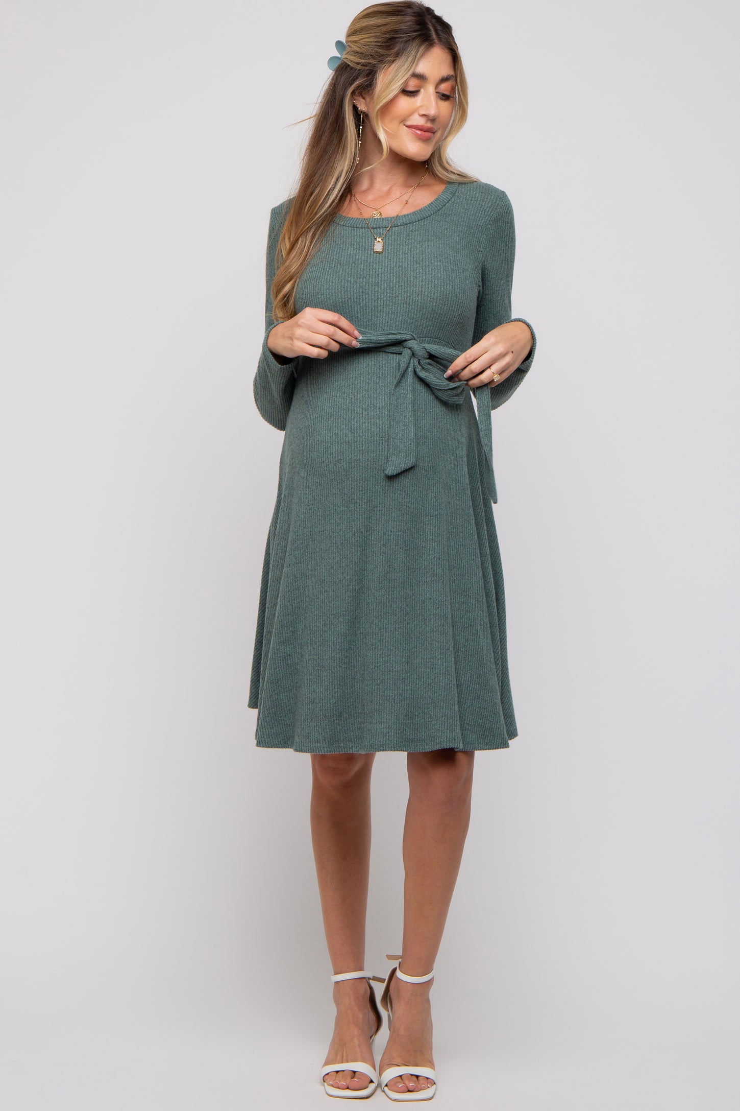 woman wearing a teal long sleeve maternity dress with a tie waist and a visible baby bump