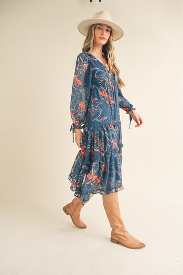 woman wearing a blue floral maxi dress with ruffles and long sleeves, paired with tan knee-high boots and a wide-brimmed hat