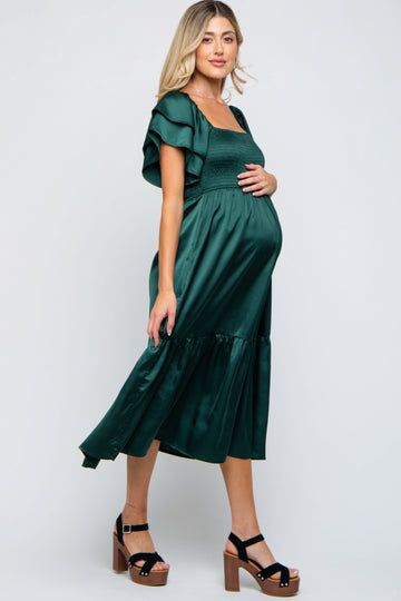 woman wearing a dark green maternity dress with flutter sleeves and a gathered waist, showing a baby bump