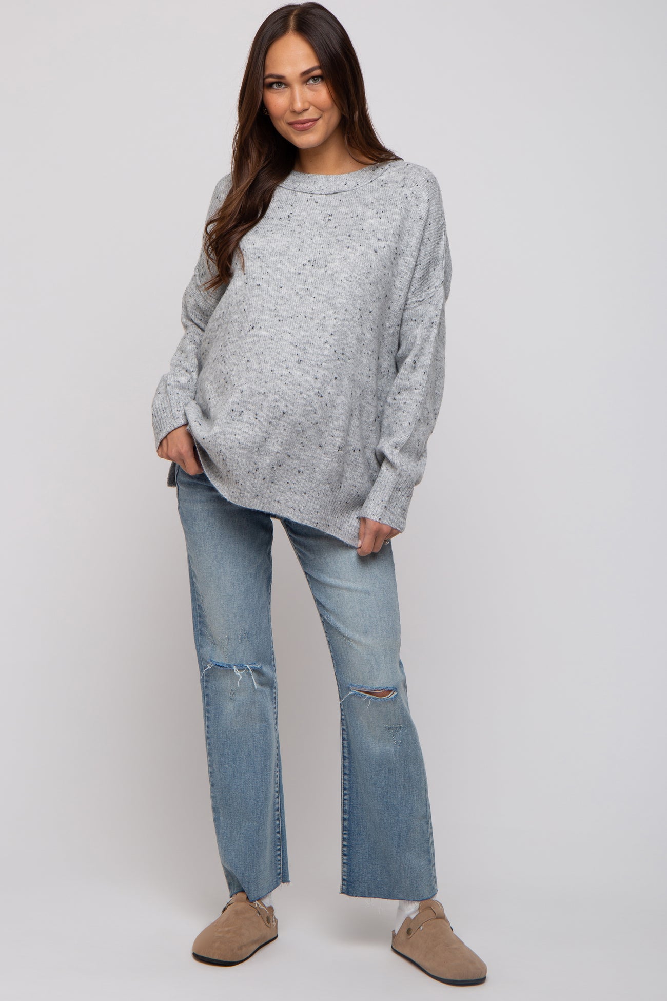 woman wearing a gray speckled oversized maternity sweater and ripped jeans, showing her baby bump