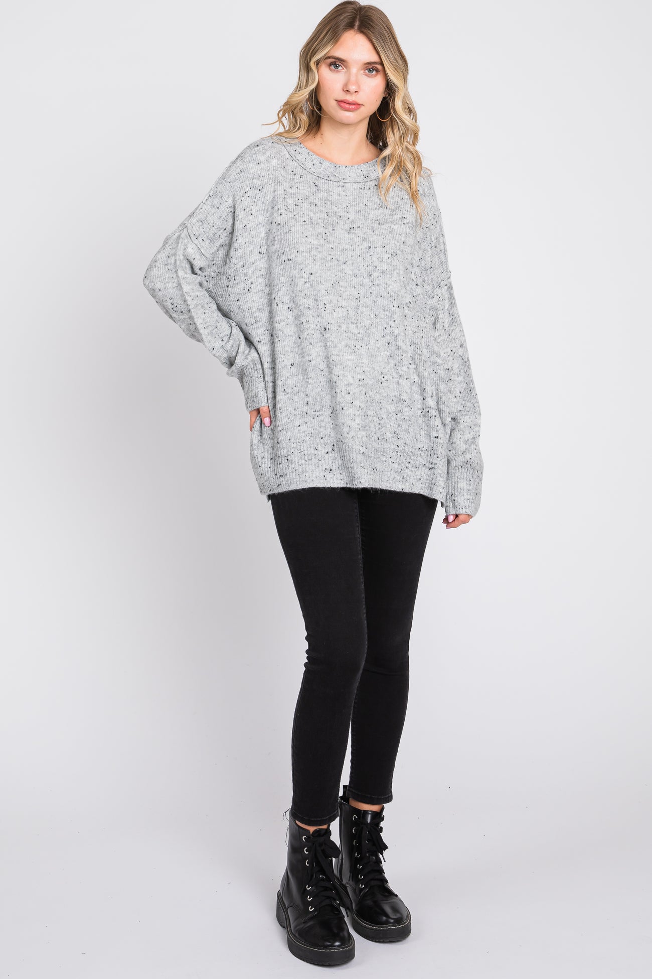woman wearing a lightweight grey oversized sweater with a loose fit and black skinny jeans, standing with one foot forward