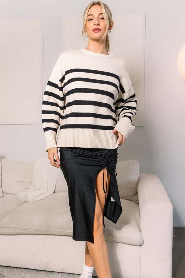 woman wearing a cream and black striped oversized sweater and a black midi skirt with a side slit