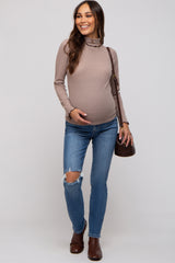 woman wearing a taupe long sleeve maternity top and distressed blue jeans, showing her baby bump with a brown handbag.