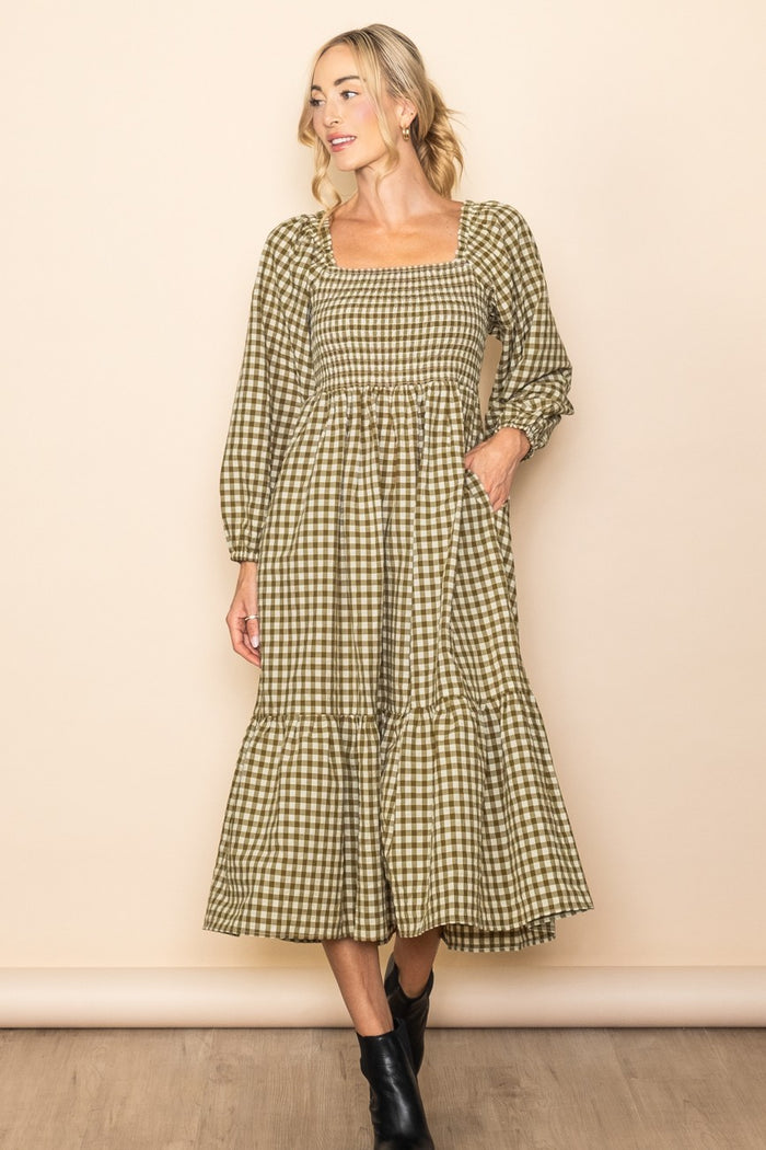 woman wearing a green and beige plaid midi dress with long sleeves and a tiered skirt, standing against a neutral background