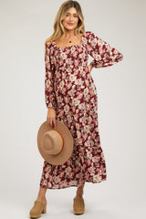 woman wearing a burgundy floral maternity maxi dress and holding a wide-brimmed hat with a baby bump visible