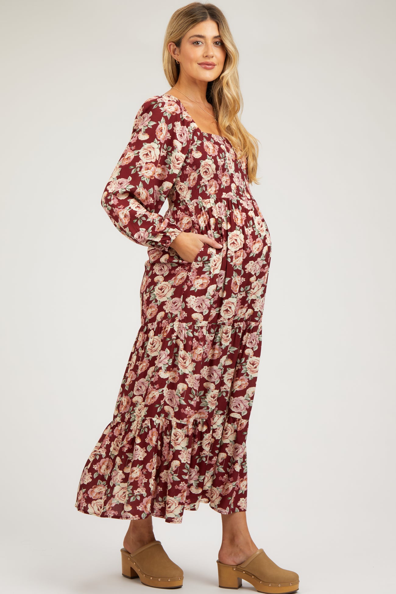 woman wearing a burgundy floral maternity maxi dress with long sleeves and pockets, showing her baby bump