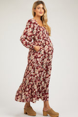 woman wearing a burgundy floral maternity maxi dress with long sleeves and pockets, showing her baby bump