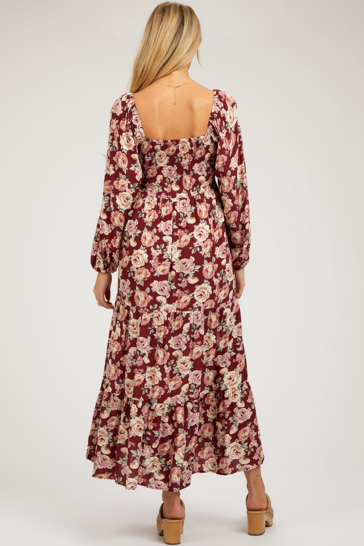 woman wearing a burgundy floral maternity maxi dress with long sleeves and a smocked bodice, showing a baby bump