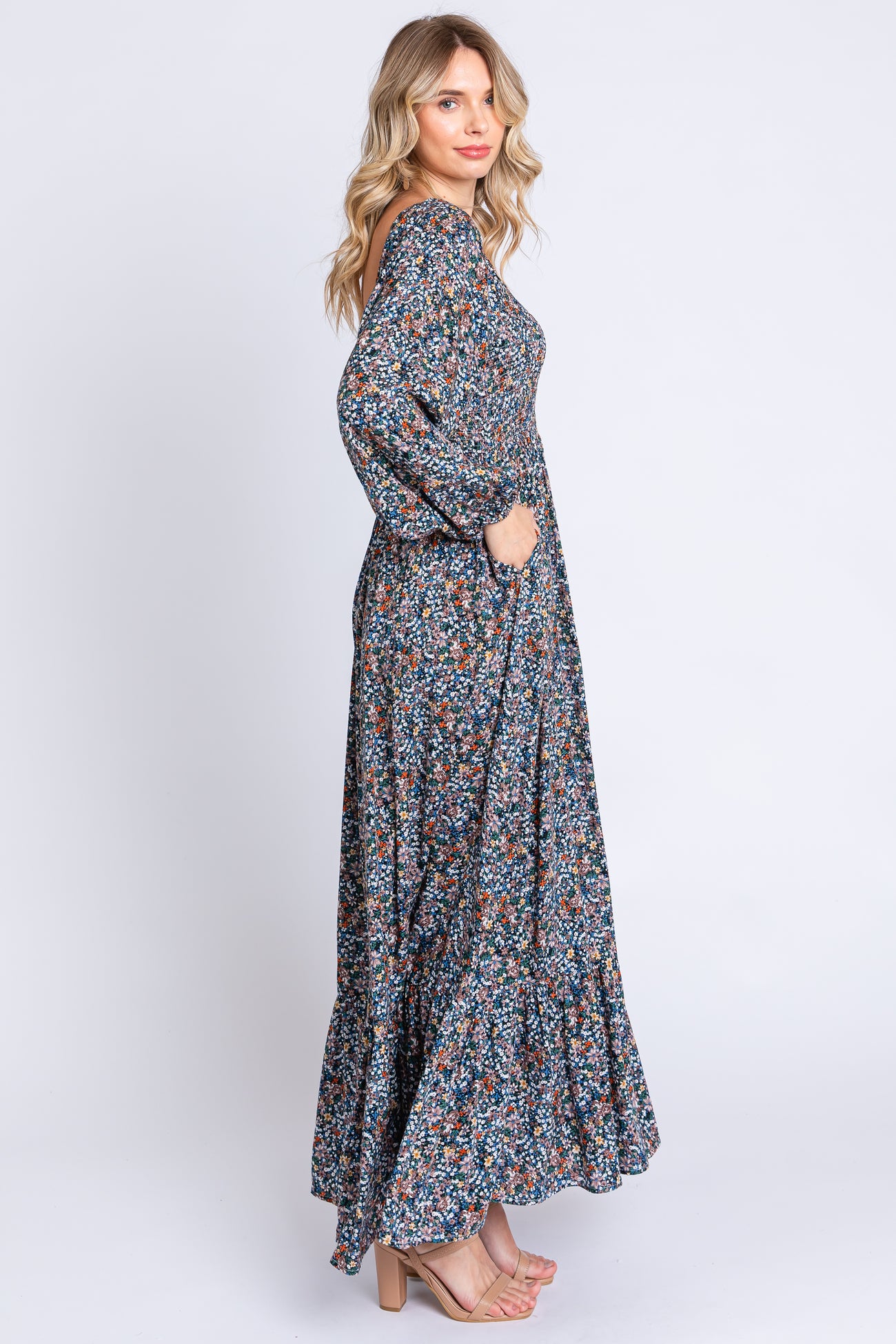 woman wearing a long floral maxi dress with long sleeves and pockets, standing in profile