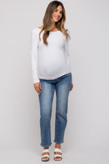 woman wearing a white long sleeve maternity top and light blue jeans, with a visible baby bump