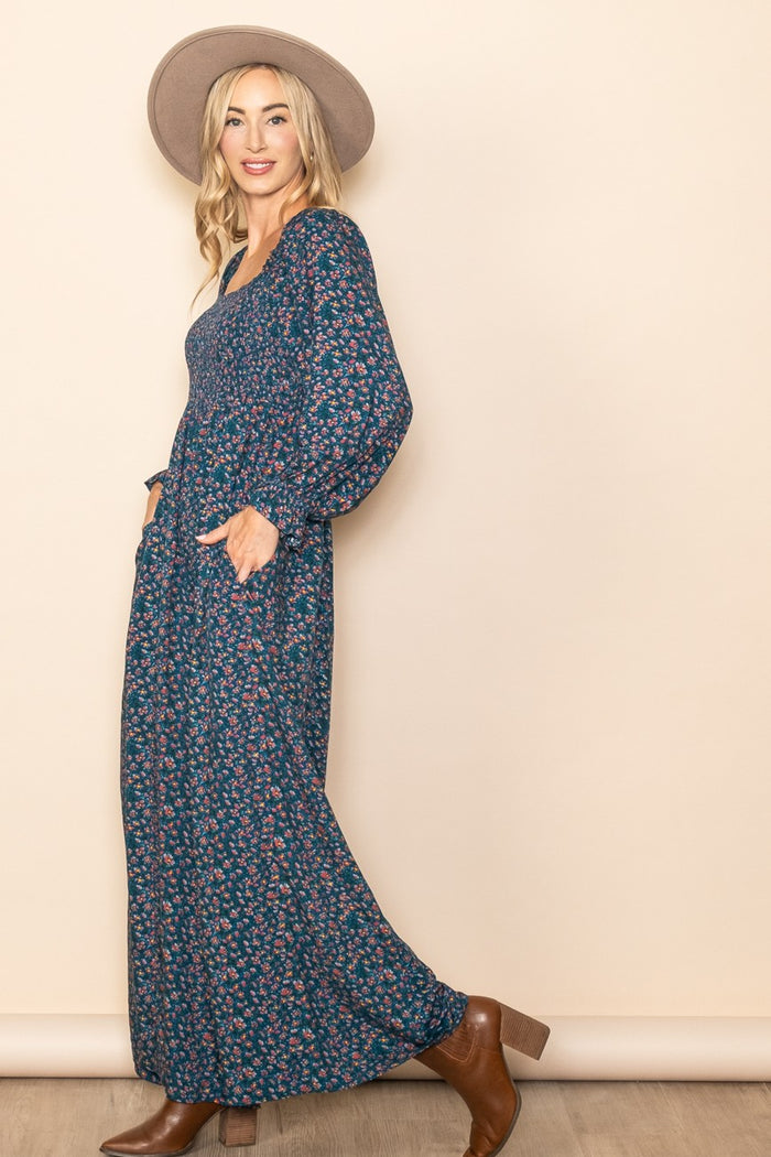 woman wearing a navy floral maxi dress with balloon sleeves and pockets, styled with a wide-brim hat and brown ankle boots