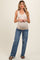 woman wearing a beige sleeveless maternity top and blue distressed jeans, showing her baby bump