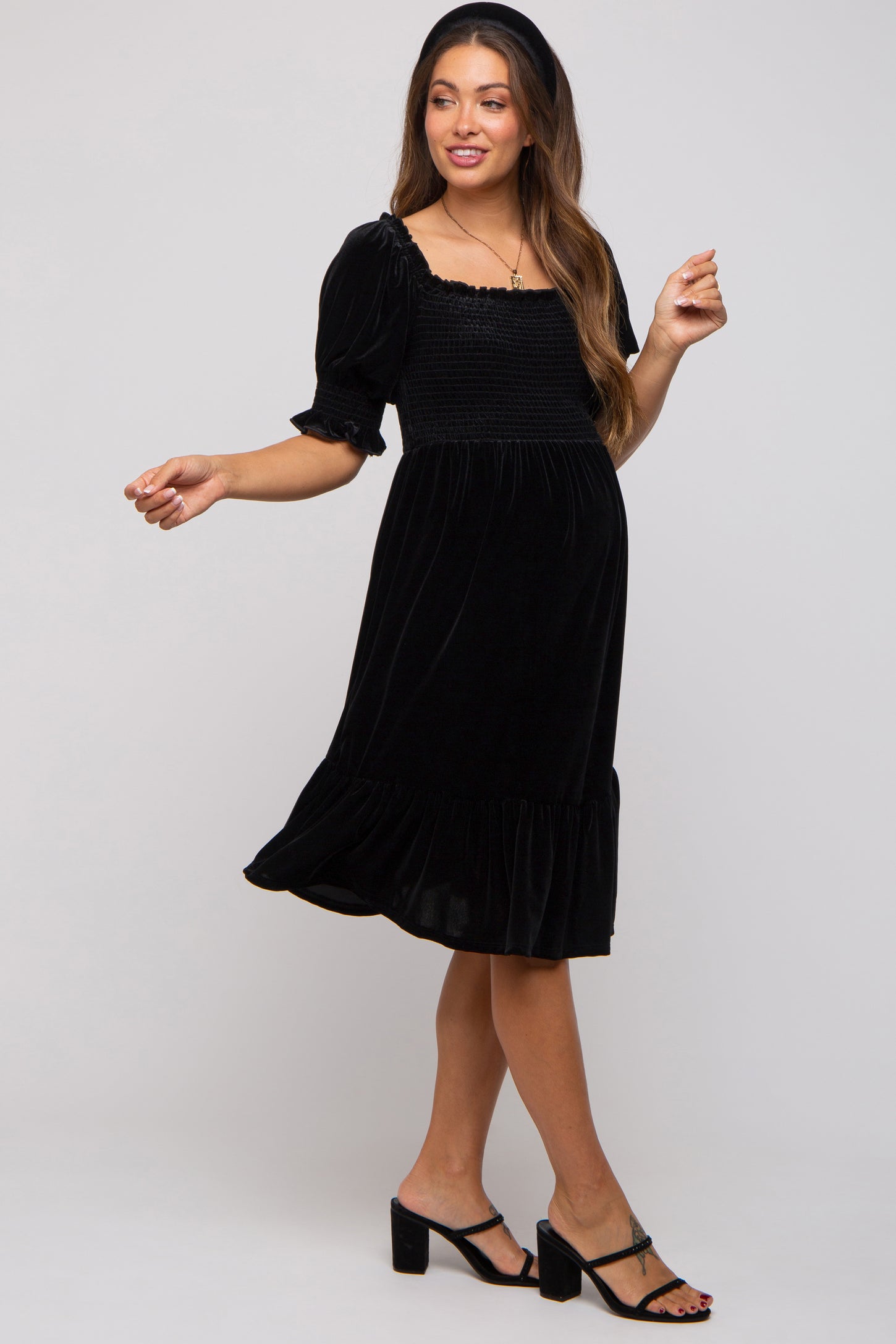 woman wearing a black velvet maternity dress with short puff sleeves and a ruffled hem, showcasing her baby bump