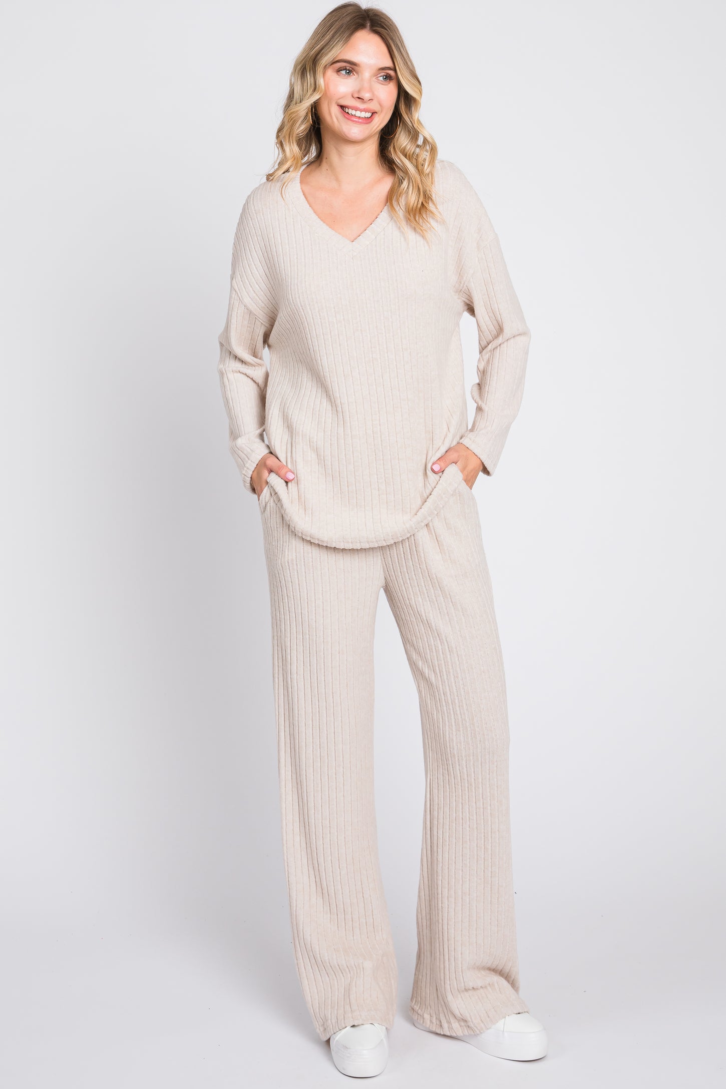 woman wearing a beige ribbed knit loungewear set with a v-neck top and wide-leg pants, posing with hands in pockets