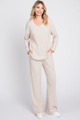 woman wearing a beige ribbed knit loungewear set with a v-neck top and wide-leg pants, posing with hands in pockets