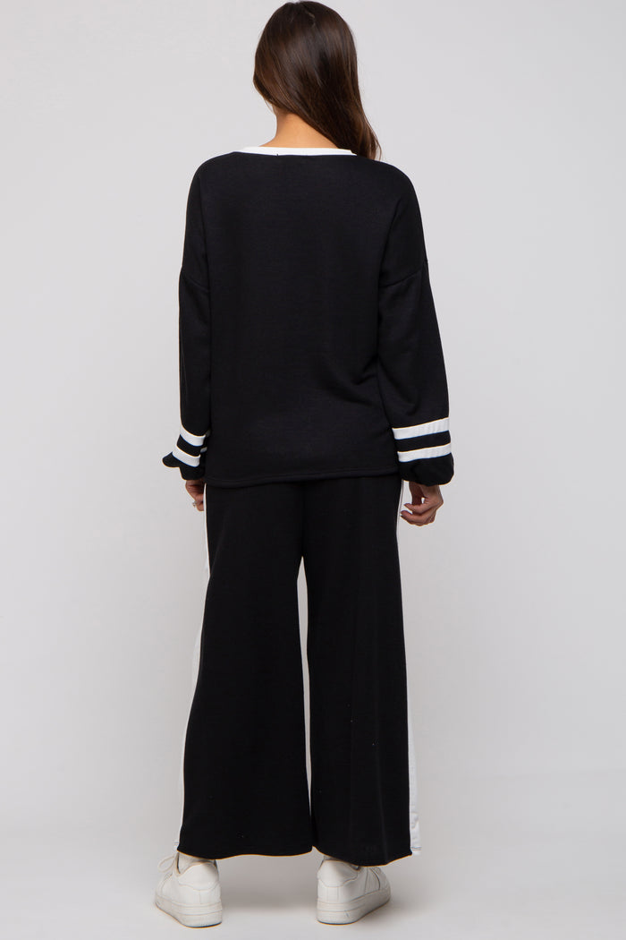 woman wearing a black maternity sweater with white stripes on the sleeves and matching black wide-leg pants