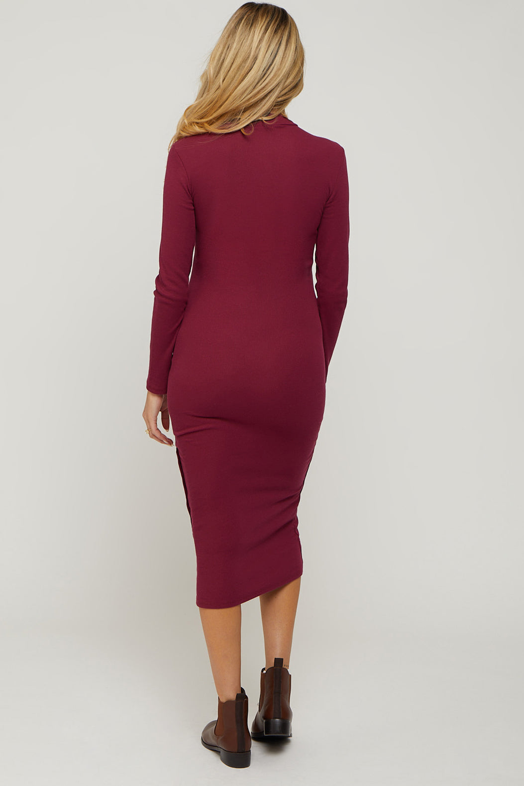 woman wearing a burgundy long sleeve fitted maternity dress with side slits and a tapered silhouette