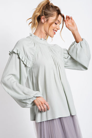woman wearing a light green long sleeve blouse with ruffled details and balloon sleeves