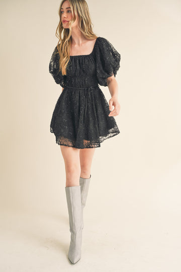 woman wearing a black lace puff sleeve mini dress with a cinched waist and silver knee-high boots