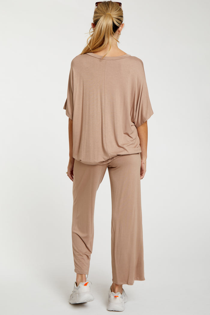 woman wearing a beige maternity lounge set with a relaxed top and wide-leg pants, showing a baby bump from the back