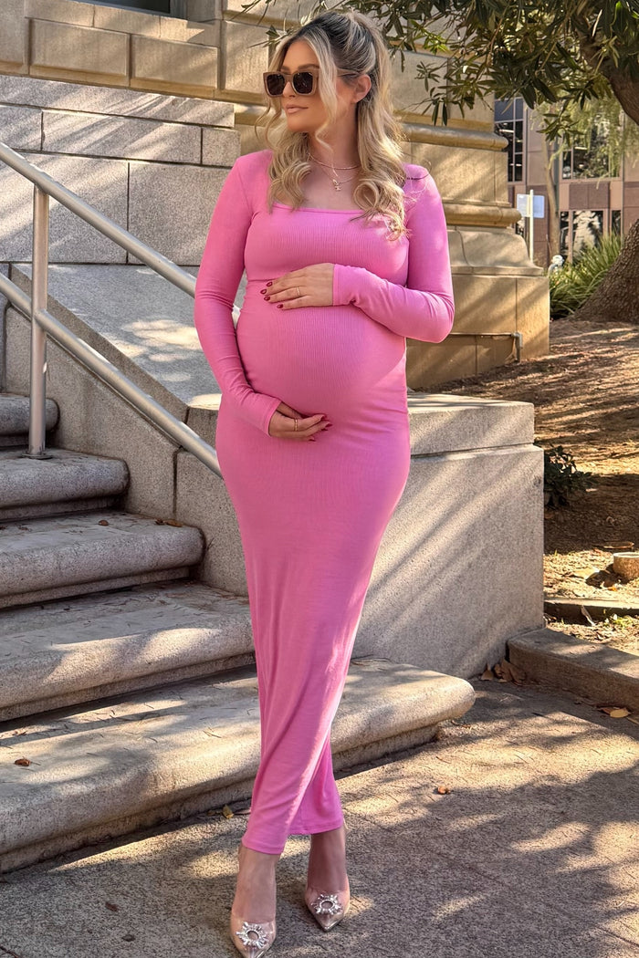 woman wearing a pink long sleeve maternity dress and holding her baby bump outdoors in sunlight