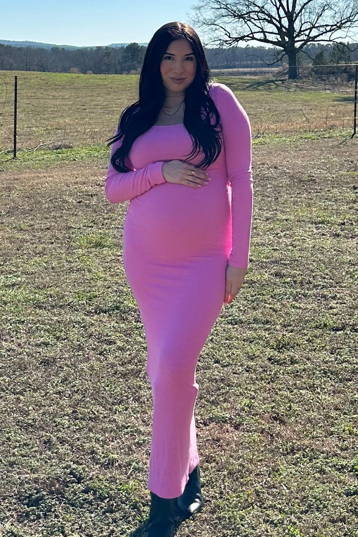woman wearing a pink long sleeve maternity dress and holding her baby bump in a field