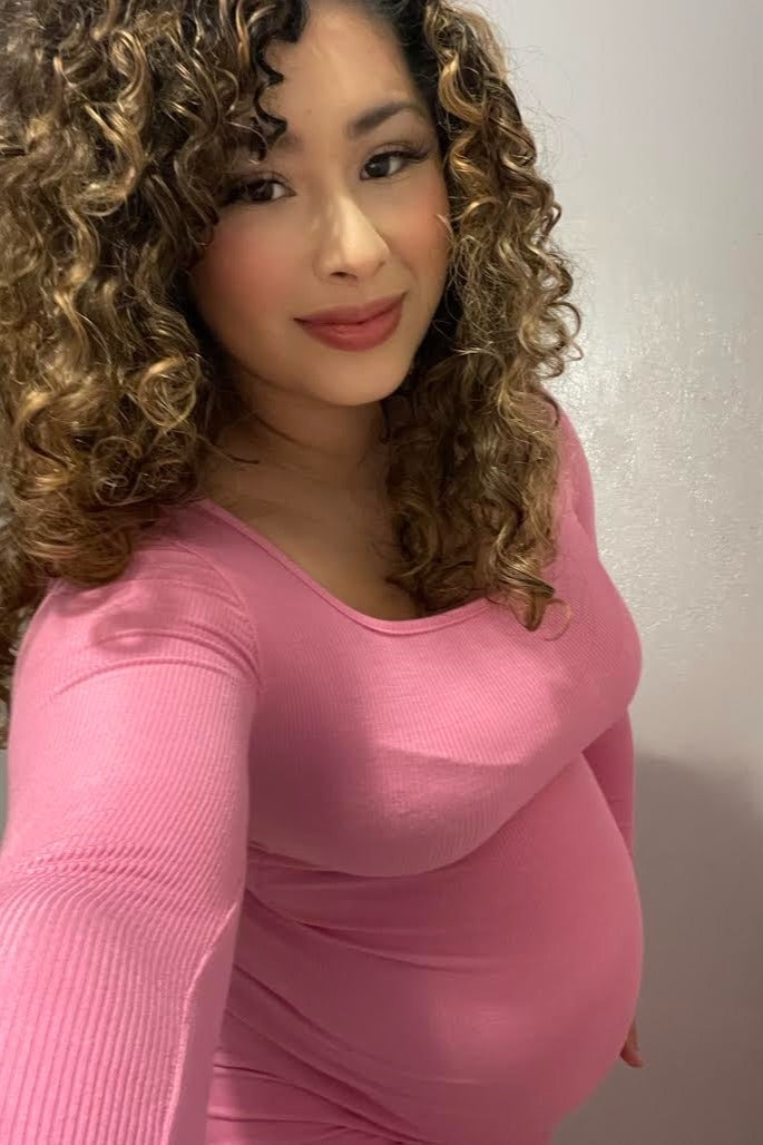 woman wearing a pink long sleeve maternity dress showcasing her baby bump