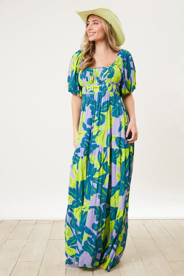 woman wearing a colorful green and blue floral maxi dress with puff sleeves and a square neckline, accessorized with a wide-brimmed hat