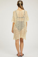 woman wearing a cream crochet maternity cover-up dress with a loose fit and short sleeves, shown from the back