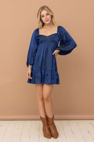 woman wearing a dark blue satin mini dress with puff sleeves and a ruffled hem, paired with brown ankle boots