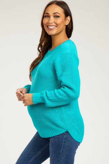 woman wearing a bright teal knit maternity sweater with a visible baby bump, paired with blue jeans