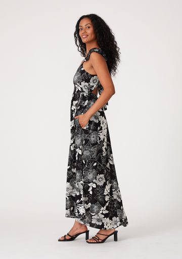 woman wearing a black and white floral maxi dress with a fitted bodice and pockets, standing sideways