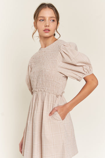 woman wearing a beige plaid puff sleeve dress with smocked bodice and side pockets