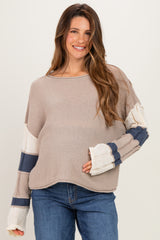 woman wearing a beige maternity sweater with multi-colored striped sleeves and showing her baby bump