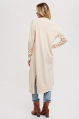 woman wearing a light pink long cardigan with side slits, standing with her back towards the camera, paired with jeans and ankle boots