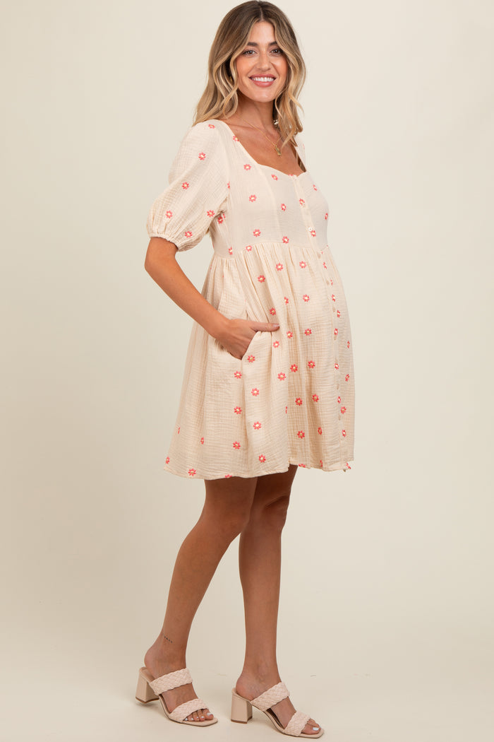 woman wearing a peach maternity dress with floral embroidery and puff sleeves, showcasing her baby bump
