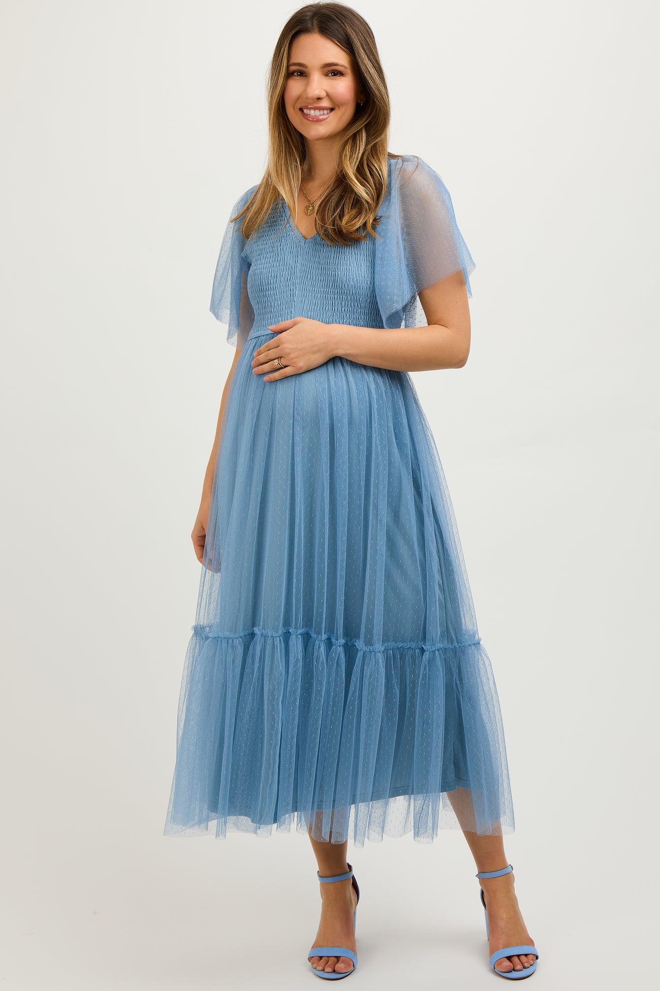 woman wearing a light blue maternity dress with short sheer sleeves and a tiered tulle skirt, holding her baby bump