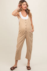 woman wearing a beige maternity overalls with button details and side pockets, showing her baby bump