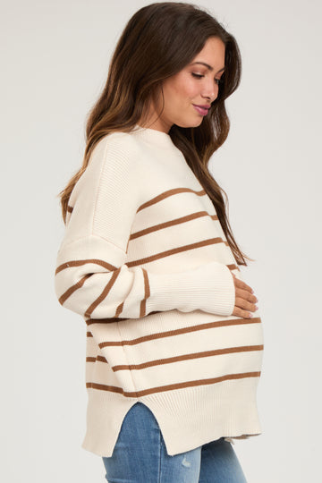 woman wearing a cream and brown striped maternity sweater, gently cradling her baby bump