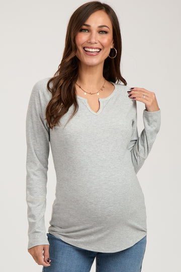 woman wearing a light gray long sleeve maternity top with a scoop neckline and smiling against a neutral backdrop