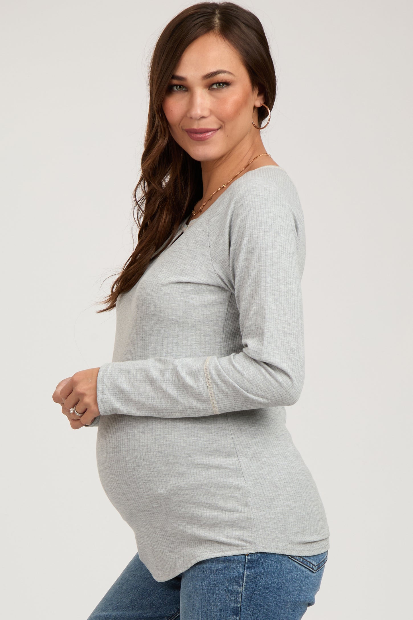 woman wearing a light grey maternity top with a fitted silhouette and a visible baby bump