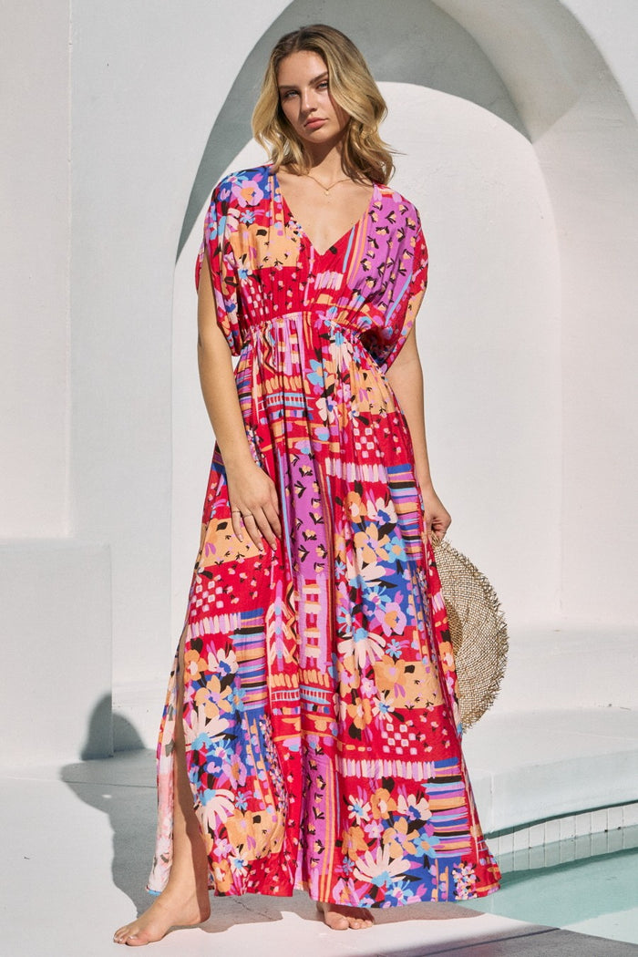 woman wearing a vibrant pink and multi-colored floral maxi dress with short sleeves and a tie waist detail