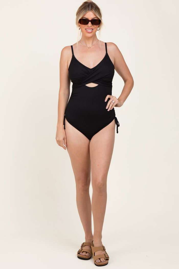 woman wearing a black ribbed one-piece swimsuit with a cutout and side ties, accessorized with sunglasses and sandals