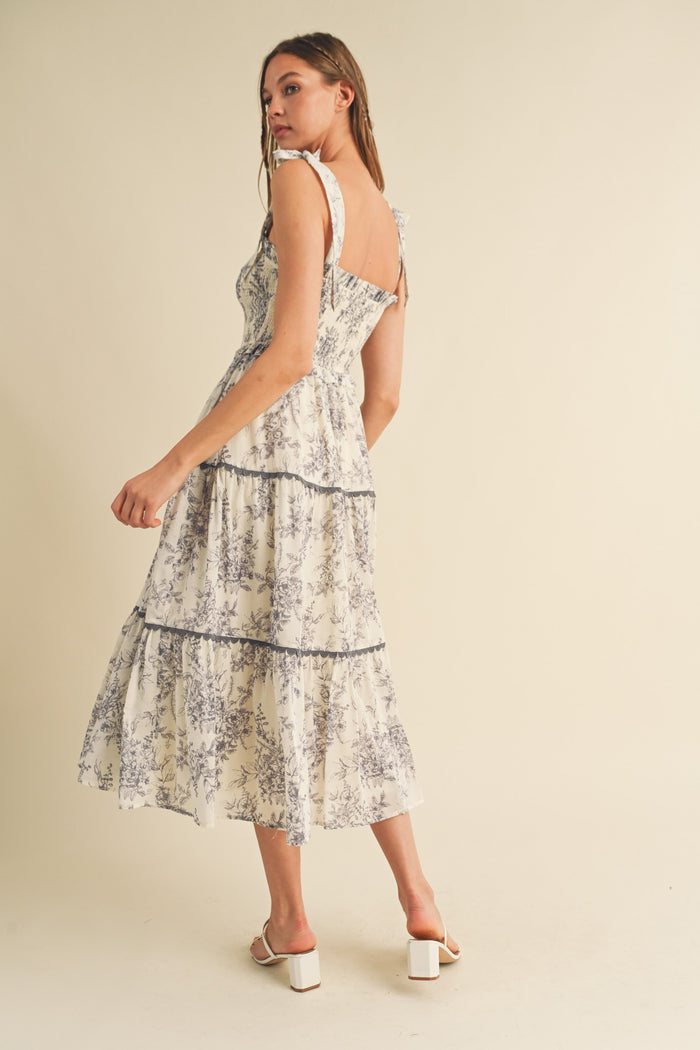 woman wearing a flowy white floral maxi dress with tiered layers and ruffled straps, seen from the back